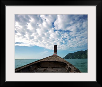 Long boat in sea with cloudy sky and mountain in background.