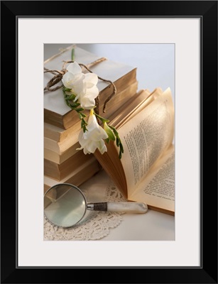 Magnifying glass beside stack of books with flowers