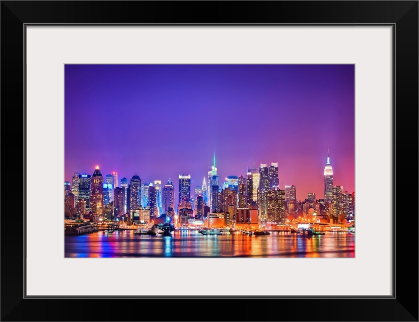 Photograph of New York skyline at night with the Hudson River in foreground.  The building lights are reflected in the water.
