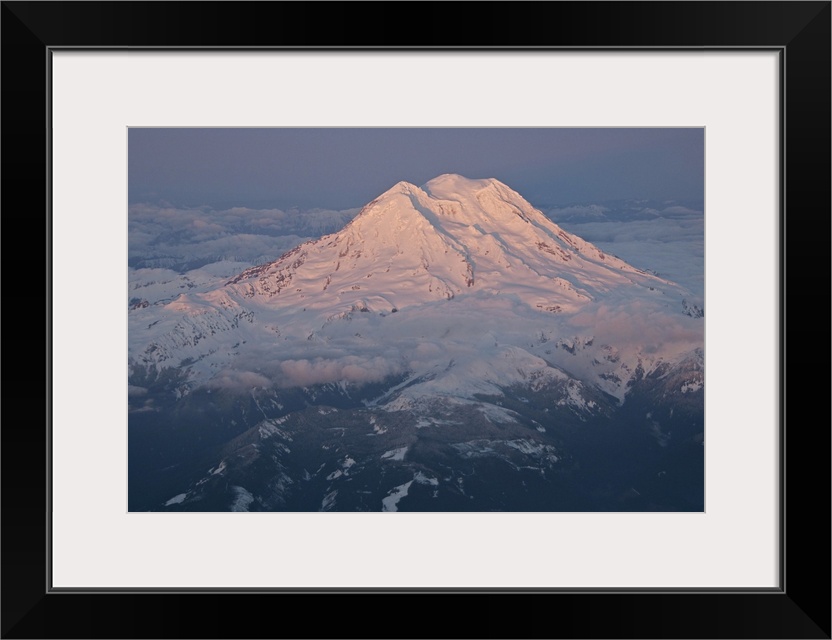 Landscape, aerial photograph of a snow covered Mount Rainier, surrounded by clouds, a dark sky in the background, in Washi...