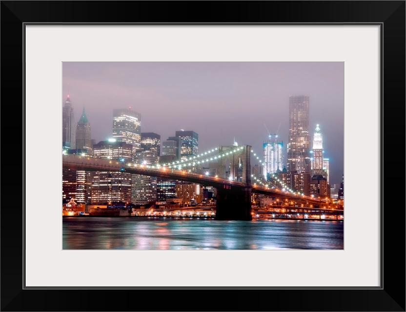 A misty night scene illuminated by urban lights of downtown Manhattan photographed from the Brooklyn shore.