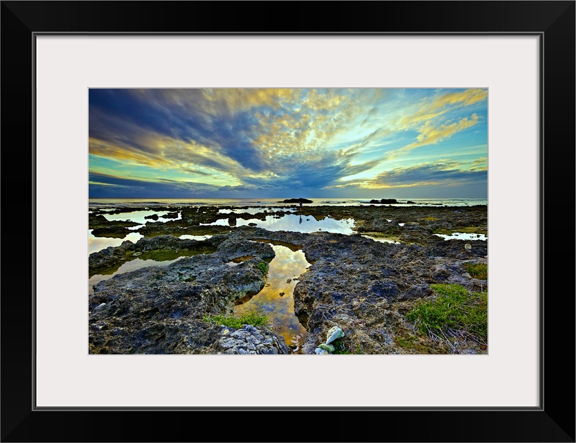 Labyrinthine coral reefs on a cloudy evening with calm water in tidal pools reflecting the sky and clouds spreading out fr...