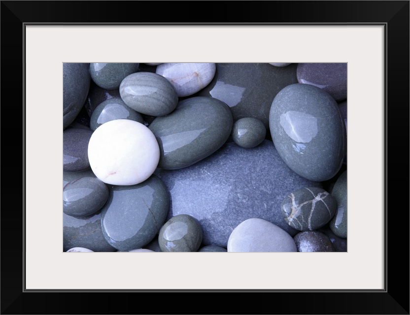 Close up photo of wet, smooth stones in varying oval shapes and gray colors.