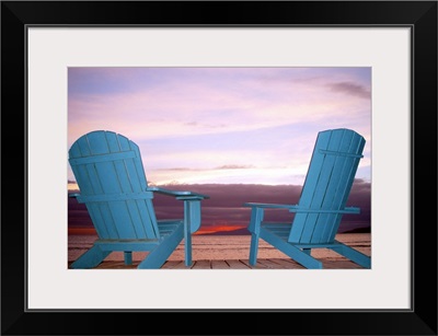 Rear view still life of two blue Adirondack chairs on a boardwalk at the coast.