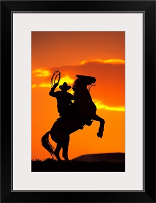 Silhouette of cowboy on horse rearing up