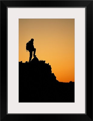 Silhouette of hiker standing on peak at sunset
