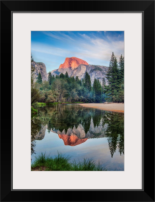 Half Dome in Yosemite National Park is reflected in the water of the Merced River at sunset.