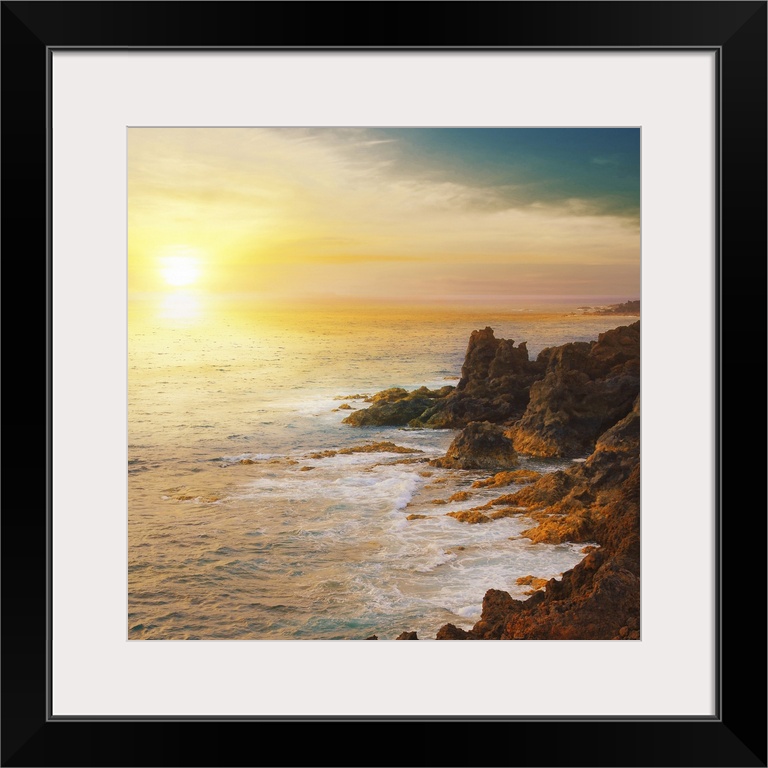 The sun is about to set below the horizon and a photograph is taken overlooking the ocean from a rocky coastline.