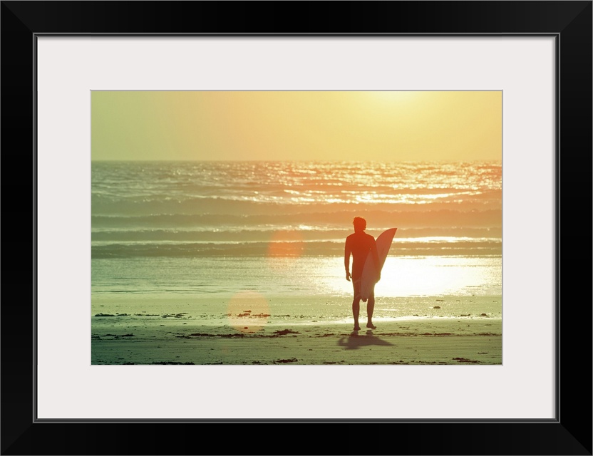 Big print on canvas of a surfer with a surfboard silhouetted against the setting sun looking out at the waves.