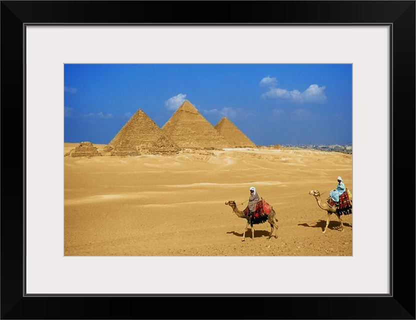 Two people riding camels near the pyramids of Giza, Egypt