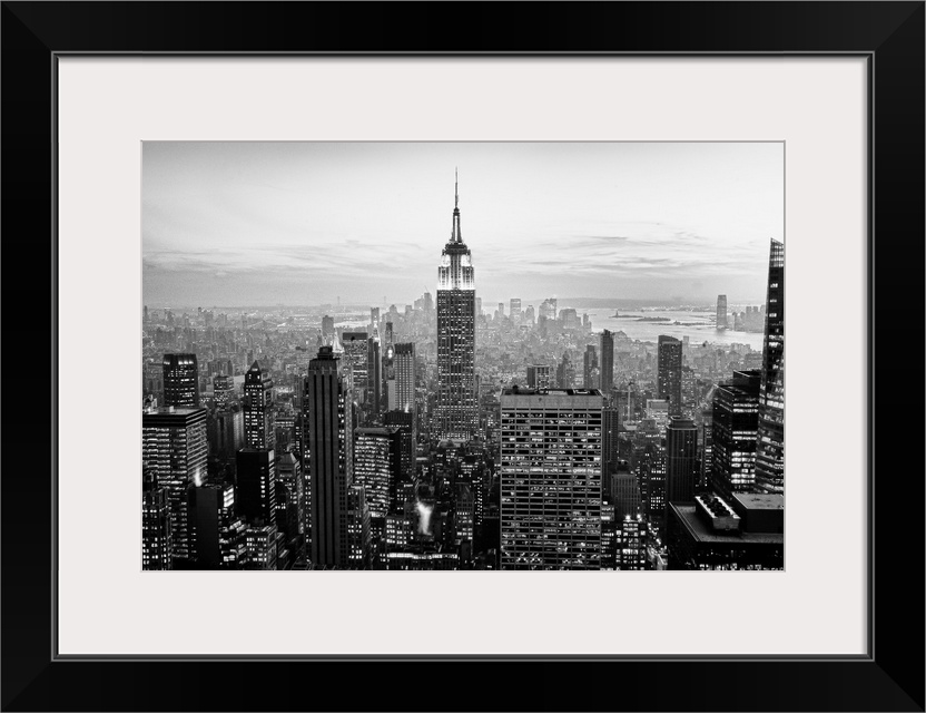 High angled photograph of city buildings at dusk.  The building windows are filled with light creating little rectangle pa...