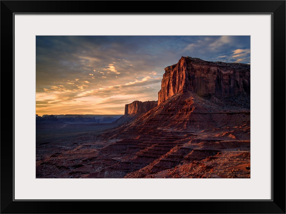 The rising sun spreads warm light across the face of Monument Valley's Mitchell Mesa.