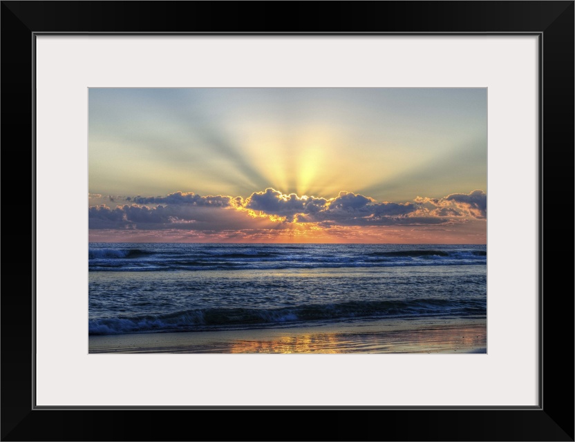 A photograph of a vibrant sunrise behind textured clouds above a restless open sea.