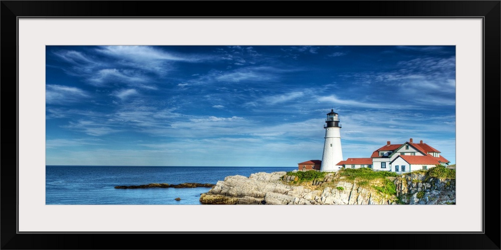 Photograph of a lighthouse on the rocky shore against a blue sky.