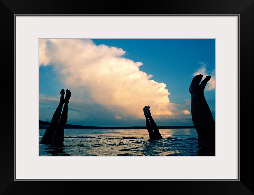 Three pairs of legs stick out of the water in Lake McConaughy, as a thunderstorm creeps forward in the distance.