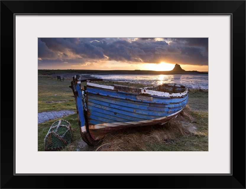 Decaying fishing boat on Holy Island at dawn, with Lindisfarne Castle beyond, Northumberland, England. Spring (March)