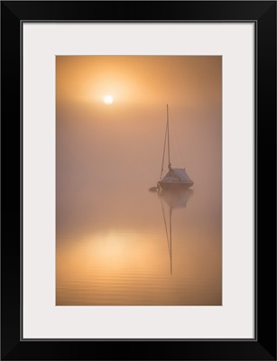 Sun rising over a sailing boat moored on a misty Wimbleball Lake, Exmoor National Park