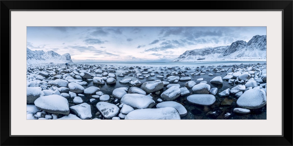 Rocks in the cold sea and snow capped mountains under the blue light of dusk Unstad Lofoten Islands Northern Norway Europe.