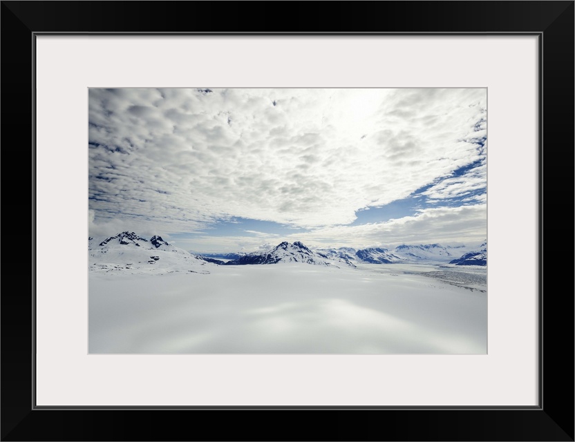 A landscape covered in snow high in the mountains of Alaska, under a cloudy sky.