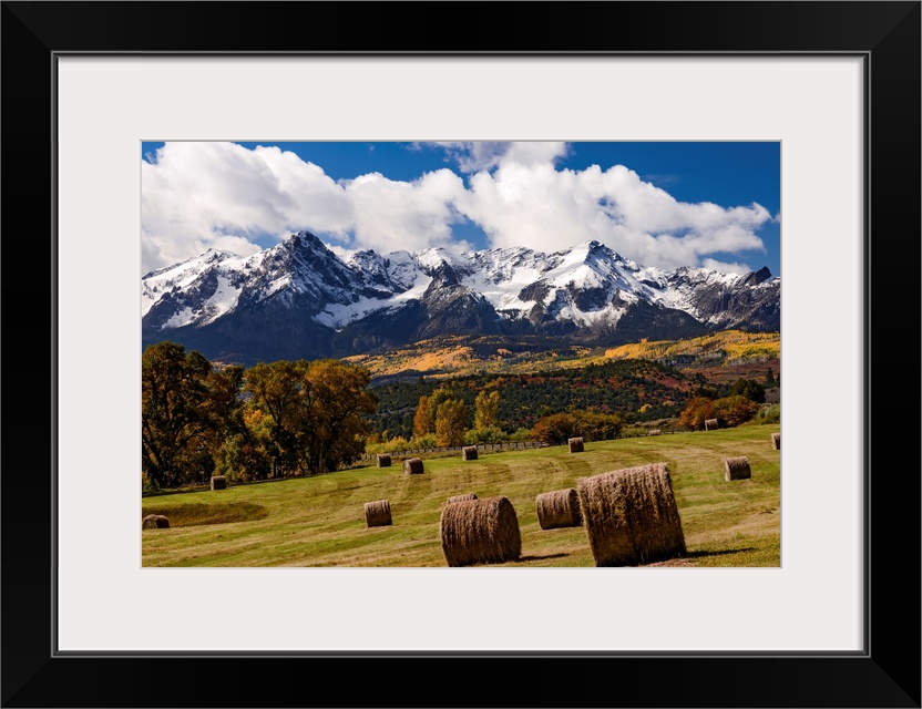 Grazing land at the foot of snow covered mountains and rustic autumn trees in a landscape photograph.