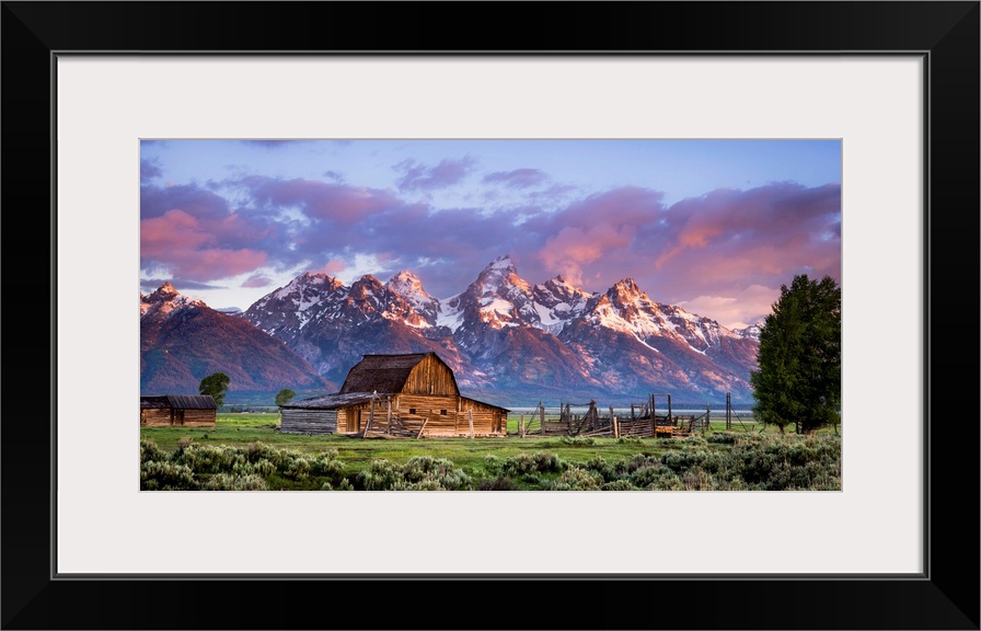 Large, horizontal photograph of an open field with an old, wooden barn and a small building next to that.  Large, snow cap...