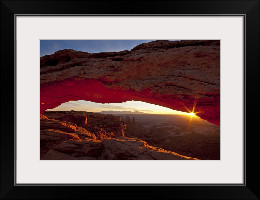 A photograph is taken through the mesa arch as the sun begins to rise over the horizon.