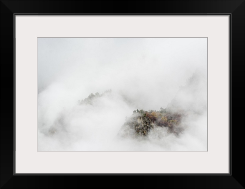 Mountainous valley with seasonally changing foliage shrouded in thick haze.