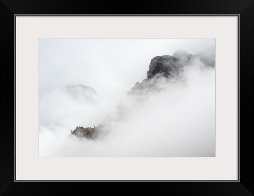 Mountainous valley with seasonally changing foliage shrouded in thick haze.