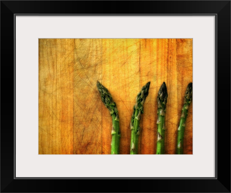 Four green asparagus spears laying on a wooden surface.