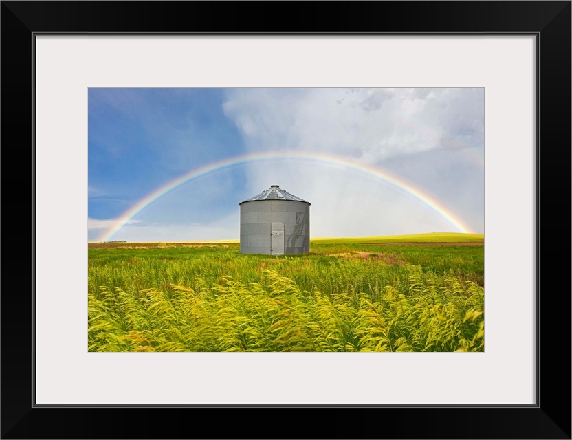 A rainbow over a grain silo and wheat field after a thunderstorm.