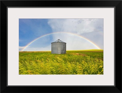 A rainbow over a grain silo and wheat field after a thunderstorm