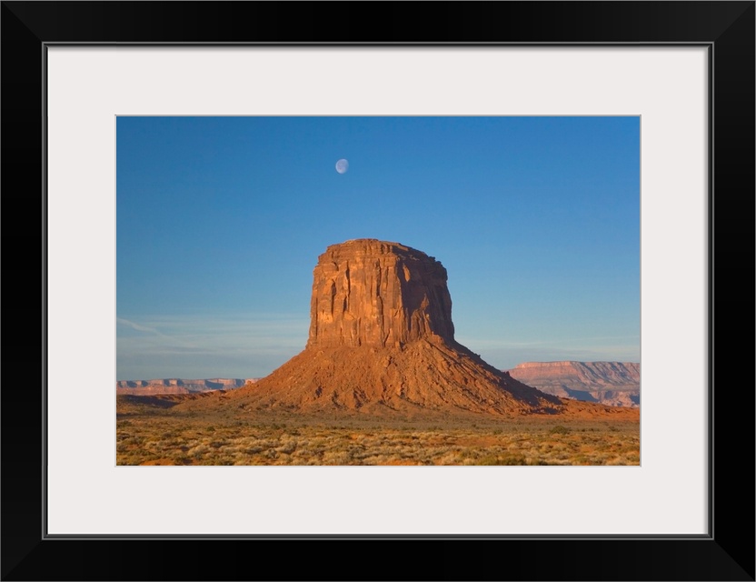 Moon visible over rock formation in Monument Valley in early morning.