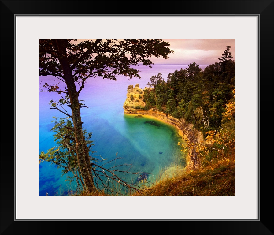 An immense cliff is covered with various trees and thick foliage that curves and overlooks Lake Superior.