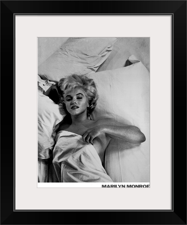 Large monochromatic photograph shows a famous American actress, model, and singer laying in bed with a blanket over her nu...