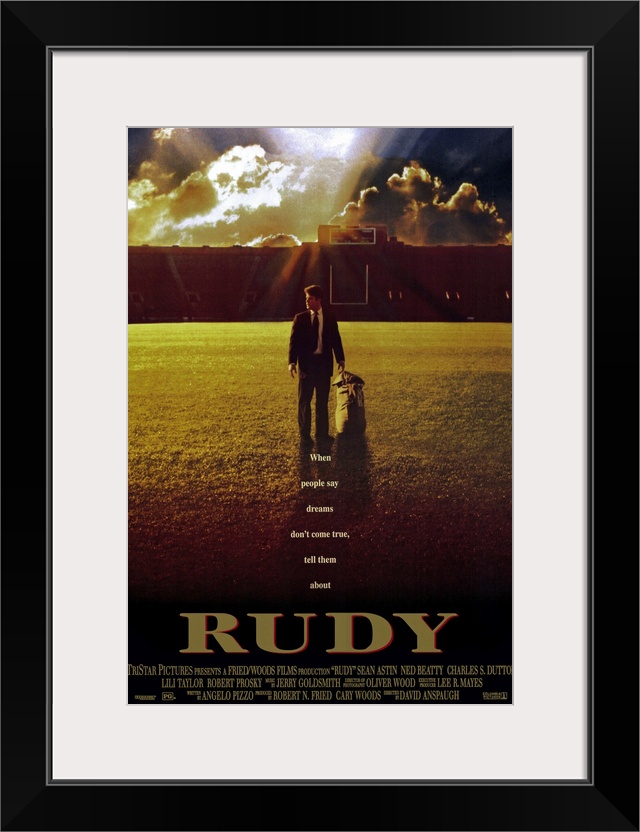 This large vertical piece is a movie poster for "Rudy". It pictures the star character walking across the football field i...