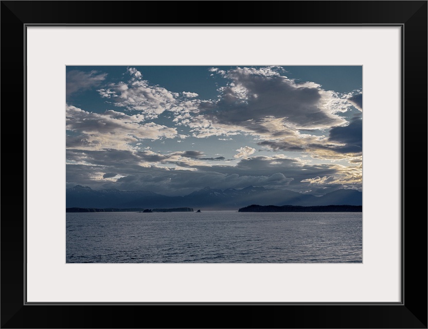 Gentle sunset with subtle God-beams surround a beautiful Alaskan snow-capped mountain range fronted by contrasting island ...