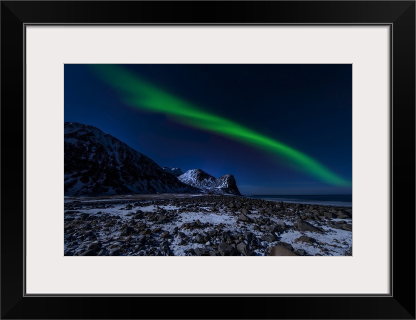 A photograph of the northern lights over a snowy rugged landscape with mountains in the distance.