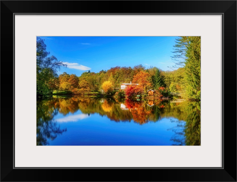 Colorful trees in the fall and a deep blue sky reflected in the calm waters of a lake.