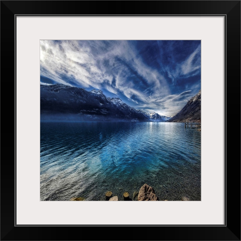 This square shaped decorative wall art is a landscape photograph of a lake surrounded by snow covered mountains beneath a ...