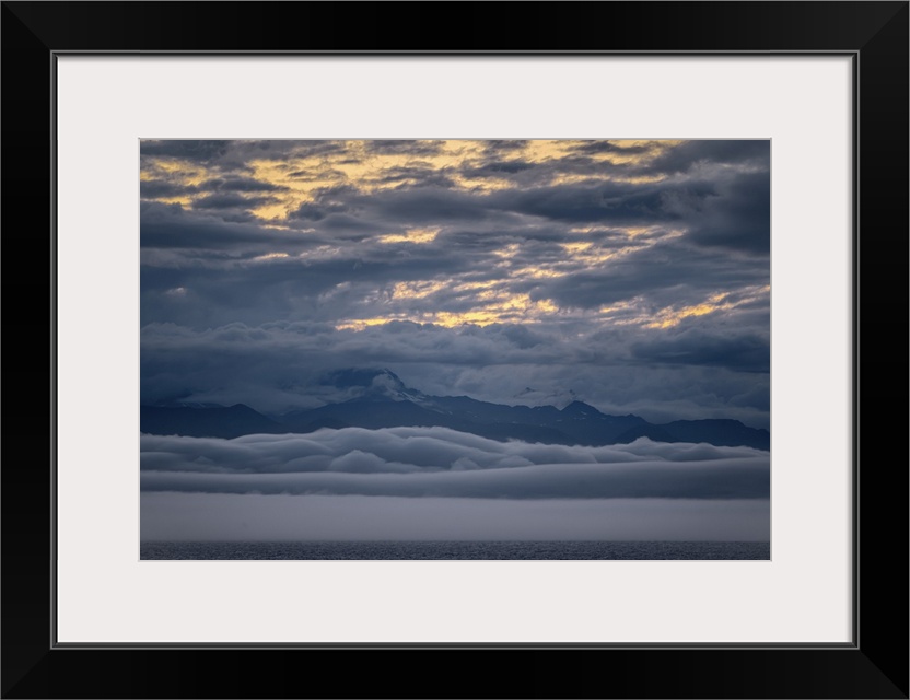 Peaceful snow-capped Alaskan mountain range at ocean's edge with clouds above and clouds below (cloud inversion) make for ...