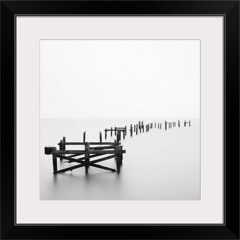 Large photograph focuses on a deteriorating dock sitting alone in a wasteland of fog.