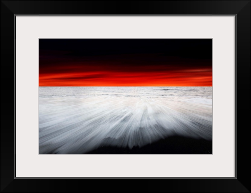 A dramatic photograph of a blazing sky hanging over a white seascape seen from a black sand beach.