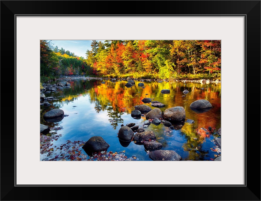 Fine art photo of bright colors of a forest in autumn being reflected in a pond full of rocks.