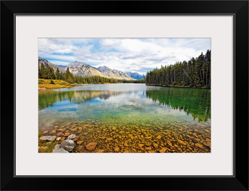 Giant photograph taken from the rocky shores of a lake that is surrounded by dense forests and snow covered mountains in t...