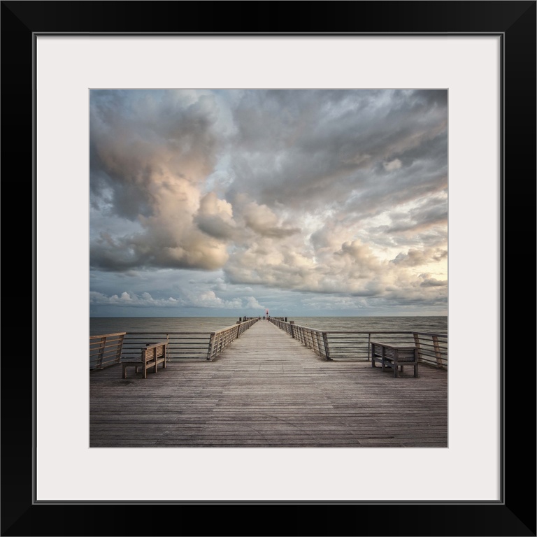 A wooden pier leading to the ocean with dramatic clouds above.