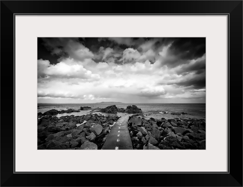 Black and white photograph of a road surrounded by coastal rocks leading into the ocean.