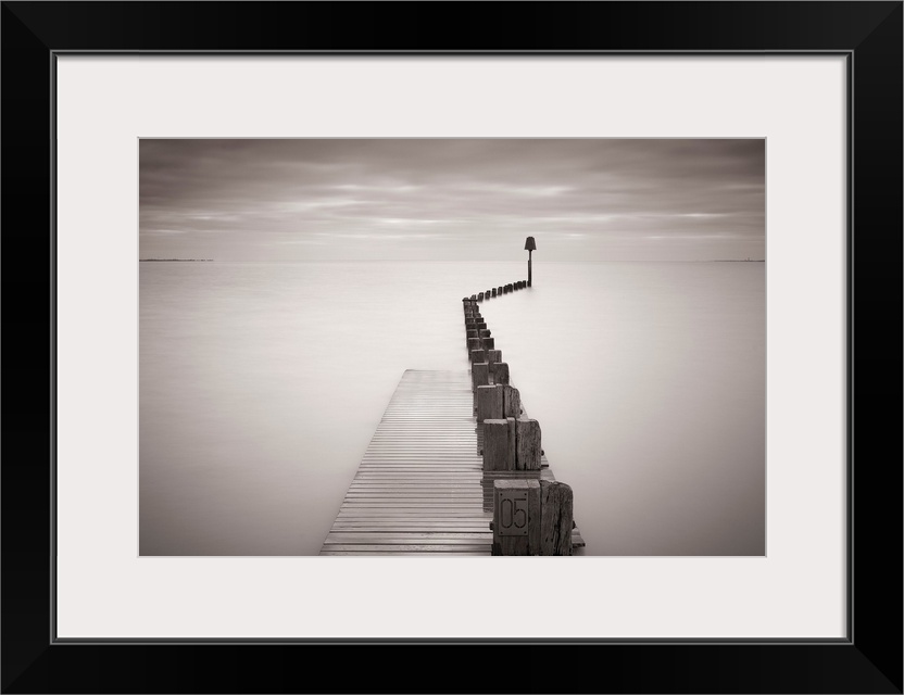 Photograph of dock stretching into ocean under a cloudy sky.