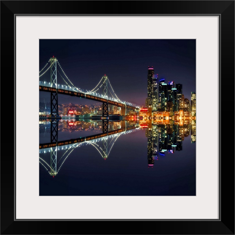 Square photograph of the Bay Bridge and downtown San Francisco lit up at night and reflecting onto the motionless water.