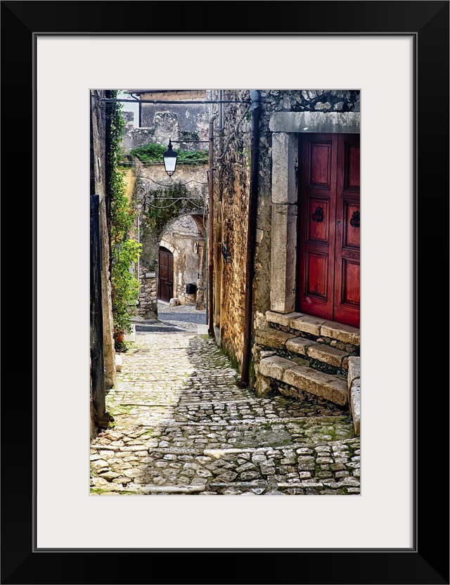 Cobblestone street in Sermoneta, Italy, with a red door on the side.