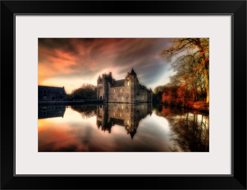 A large castle sits right on the water and reflects perfectly just below. The sunset glows in the sky and reflects into th...